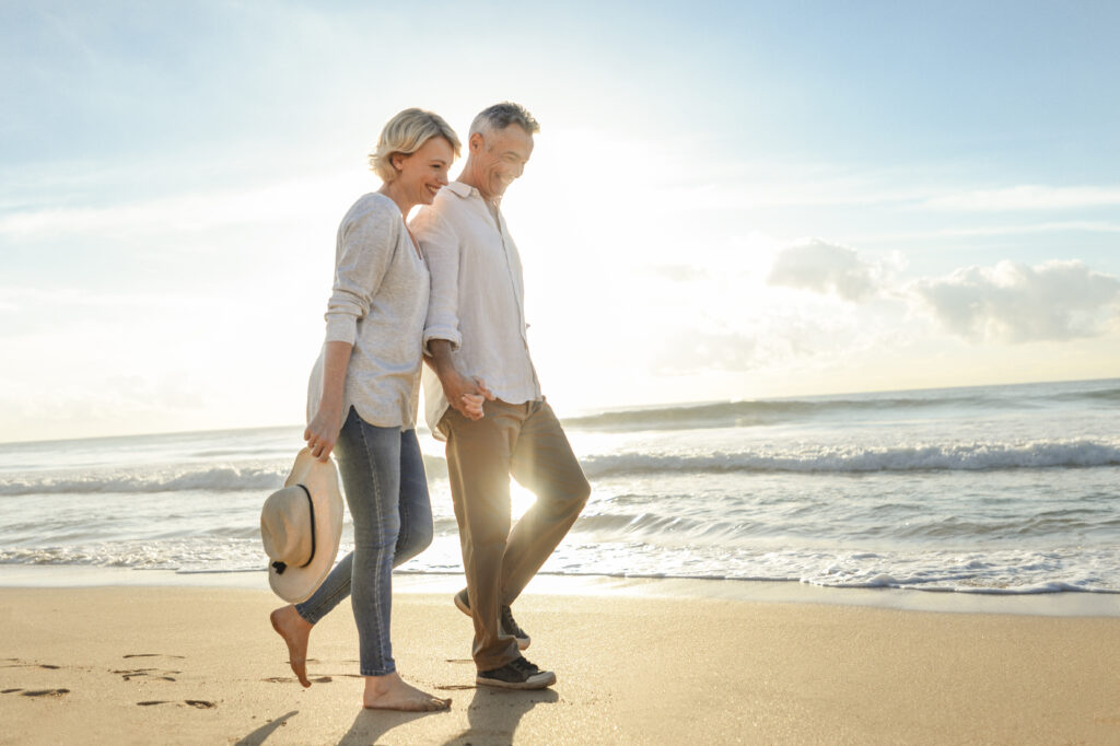 Mature couple walking on the beach at sunset or sunrise.