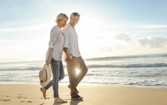 Mature couple walking on the beach at sunset or sunrise.