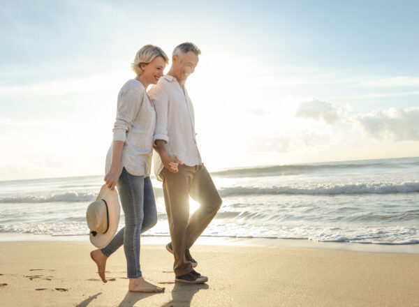 Mature couple walking on the beach at sunset or sunrise.
