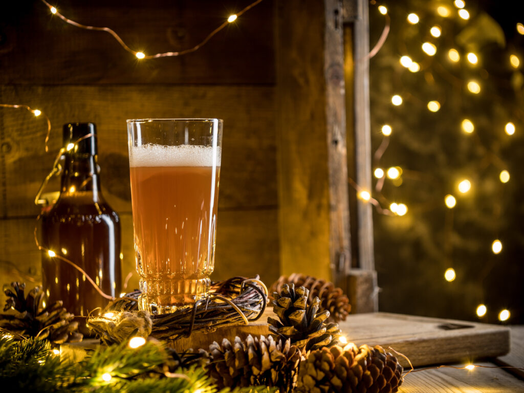 Beer in glass on wooden background with Christmas lights and pine cones. 
