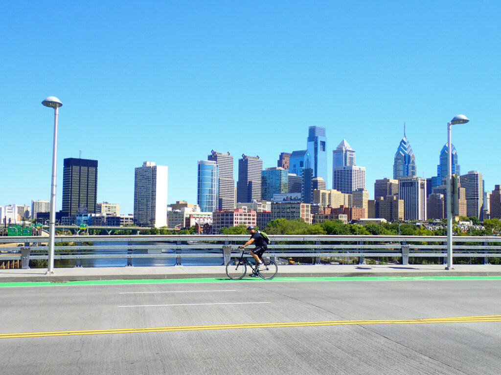 Bicyclist on the South Street Bridge with the Philadelphia Skyline behind him.