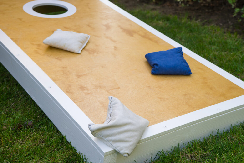 Cornhole game board leisure activity with blue and white bean bags outdoors on green grass.