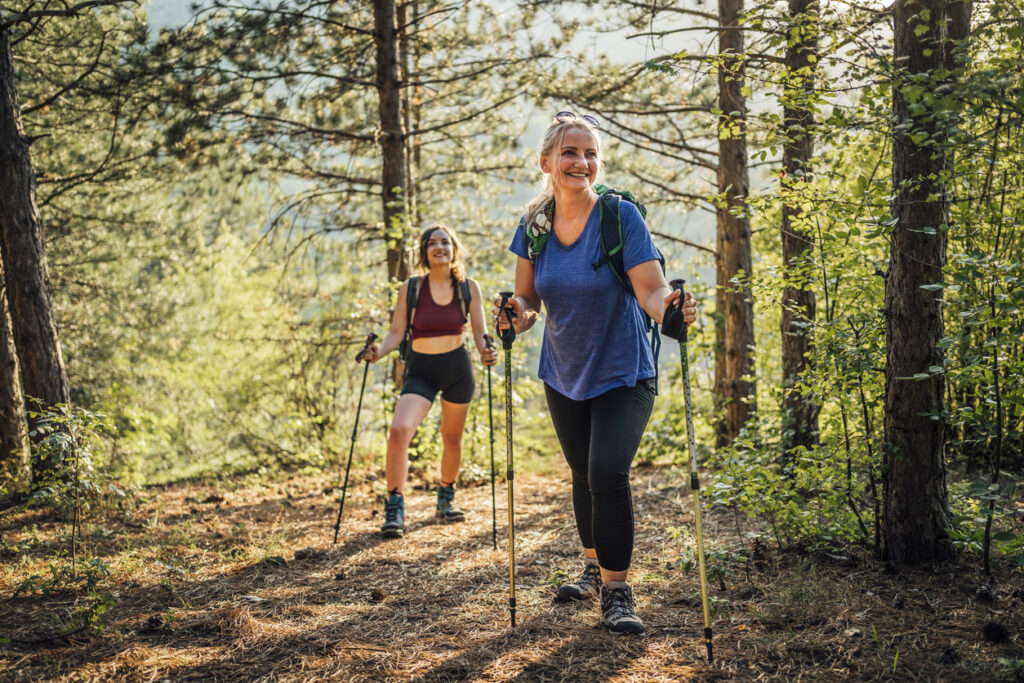 Mother and daughter with trekking poles crossing mountain forest stream