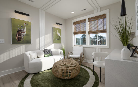 A bright, modern sitting room with a white sofa, two chairs, a round wicker coffee table, a green circular rug, and nature-themed wall art. Large windows with bamboo shades let in natural light.