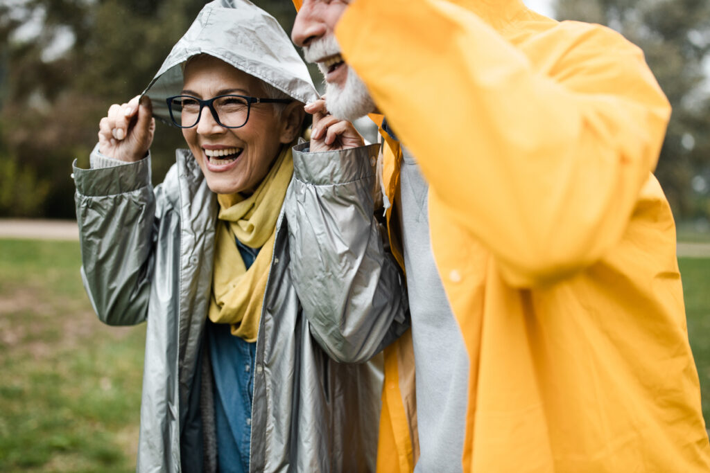 Happy mature couple covering their heads with hood during autumn day in the park.