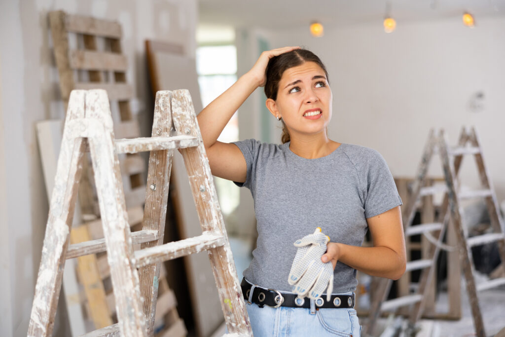 Portrait of annoyed young woman standing at stepladder in home during repair works 