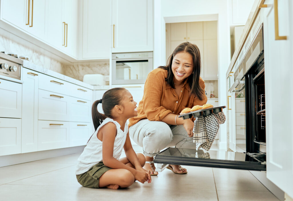 Asian, mom and girl in kitchen at oven, baking and cupcakes with stove, happy and home