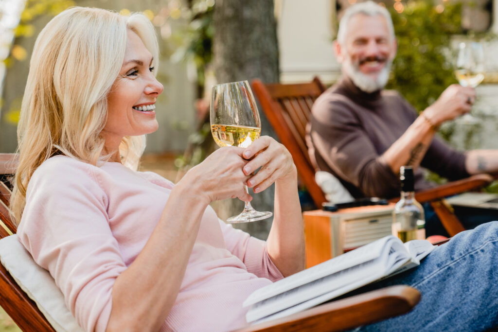 Satisfied senior woman holding a glass of wine talking with her grey-haired husband in the garden
