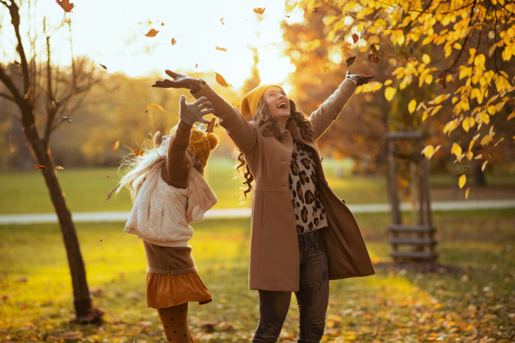 Hello november. happy modern mother and child in yellow hats outdoors in the city park in autumn rejoicing.