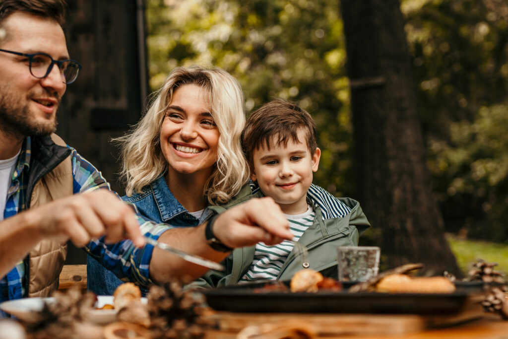 Happy two-generation family talking while enjoying food in a wooded backyard