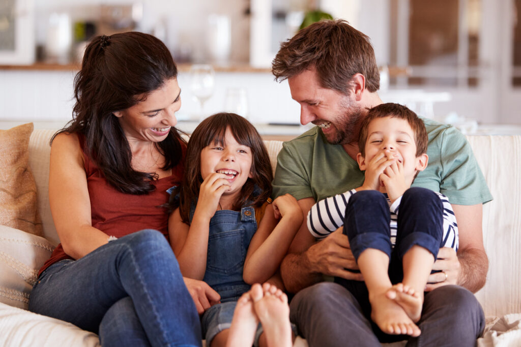 adult white couple and their two young children sitting on a sofa at home smiling at each other