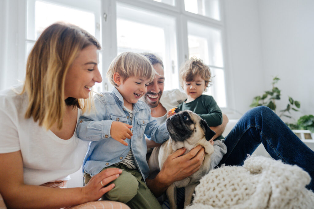 Photo of a young family with two kids playing with their cute little dog in the living room