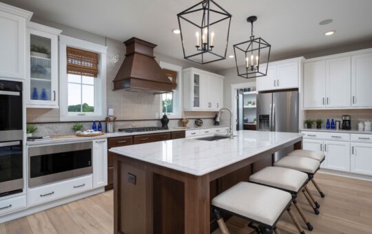 Modern kitchen with white cabinets, stainless steel appliances, a large marble island with a dark wood base, three cushioned stools, pendant lights, and windows with bamboo shades.