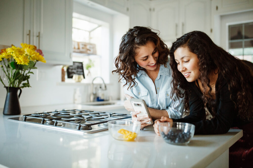 mom and daughter looking at a phone together in the kitchen