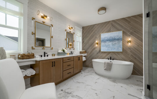 Modern bathroom with wood cabinets, double sinks, and large mirrors on the left; a white freestanding bathtub with a towel, wall art, and two sconces on a wood-textured accent wall; marble floor and bright natural light.