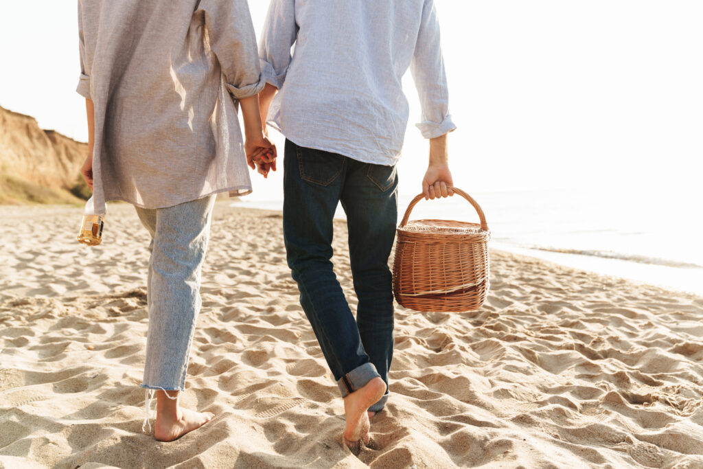 a couple walking barefoot on the beach with a picnic basket