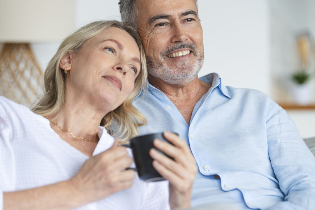 Happy mature couple at home. The woman is holding a cup of coffee. Both are happy and smiling.