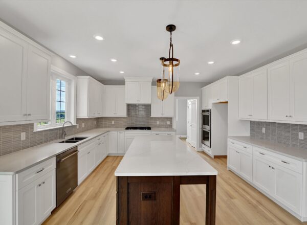 Modern kitchen with white cabinets, light wood flooring, a large island with a marble countertop and dark wood base, stainless steel appliances, a window above the sink, and pendant lighting above the island.