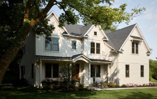 A two-story modern farmhouse with white siding, black window frames, and a dark gray roof, surrounded by green grass and landscaping—perfect for those looking to buy a home in the Philadelphia suburbs on a sunny day.