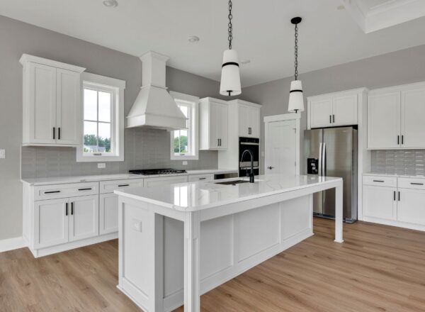 Modern kitchen with white cabinets, a large island with a sink, stainless steel appliances, pendant lights, gray tile backsplash, light wood flooring, and two windows above the stove area.