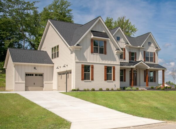 A modern two-story house with cream siding, black roof, brown shutters, a single-car garage, large windows, and a well-maintained lawn on a sunny day.