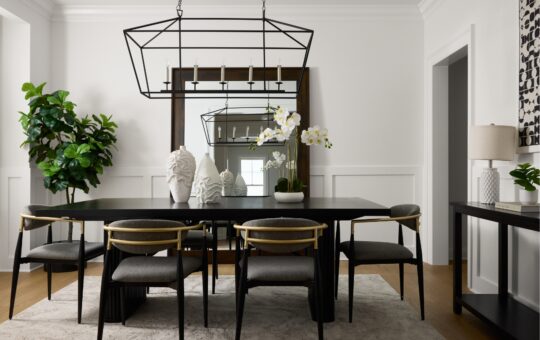 Modern dining room with black table, six chairs, large geometric chandelier, wall mirror, potted plant, and contemporary decor. Neutral tones and minimalistic design create a clean, elegant atmosphere.