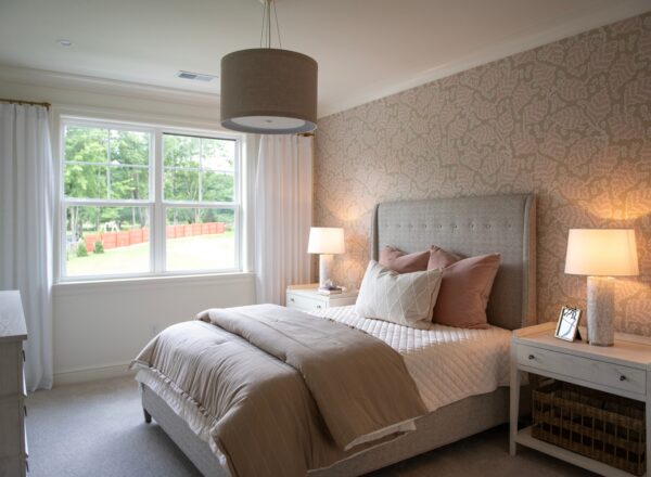 A cozy bedroom with a large window, upholstered bed with neutral bedding, two bedside tables with lamps, and patterned wallpaper. Natural light brightens the room.