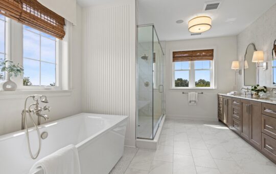 Modern bathroom with a freestanding bathtub, glass shower, double vanity with mirrors, marble tile floor, and large windows with wooden blinds letting in natural light.