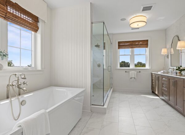 Modern bathroom with a freestanding bathtub, glass shower, double vanity with mirrors, marble tile floor, and large windows with wooden blinds letting in natural light.