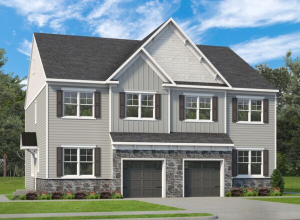 A modern two-story duplex with gray siding, white trim, dark shutters, and two garages. The front has stone accents, multiple windows, landscaped bushes, and a driveway, with trees and a cloudy sky in the background.
