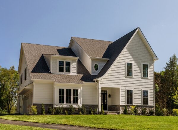 Modern two-story white house with a gray roof, large windows, and a well-kept lawn, surrounded by trees on a sunny day.