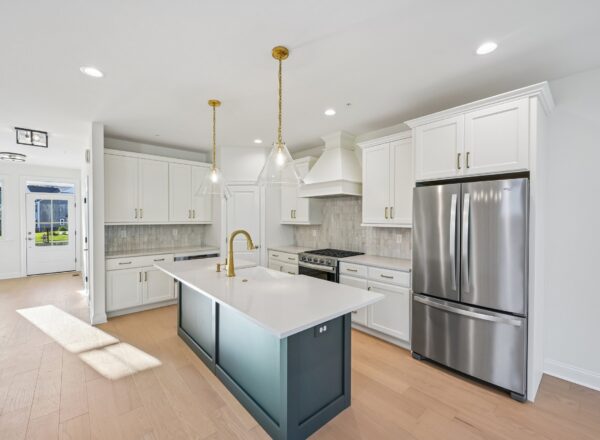 Kitchen with white cabinets, a dark blue island with a gold faucet, stainless steel refrigerator, and two glass pendant lights above the island.